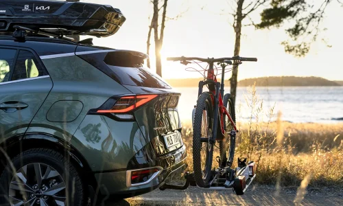 KIA-bil fotad nära med dragkrok och cykelhållare i fokus, motljus vid en sjö